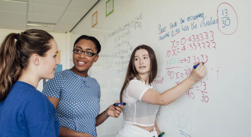 A group of students watching as one person writes a math solution on the whiteboard