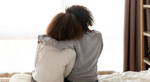 Two people sitting and embracing, one having her hand over the other